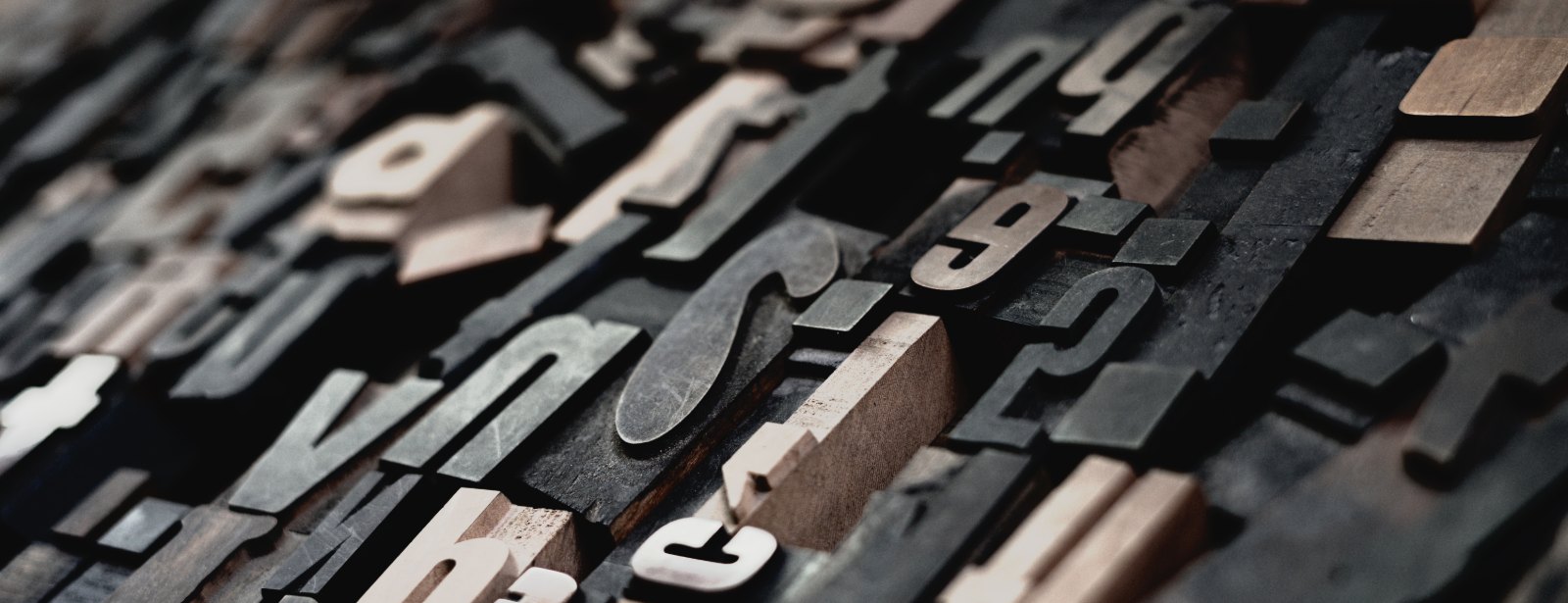 Wooden letters of many sizes lie tilted in close rows, their raised faces catching soft light.