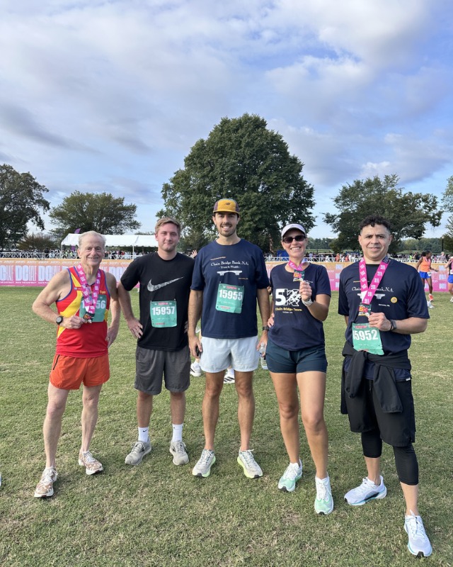 Five Chain Bridge Bank, N.A. employees with finisher medals on the grass at West Potomac Park after a 5K race.