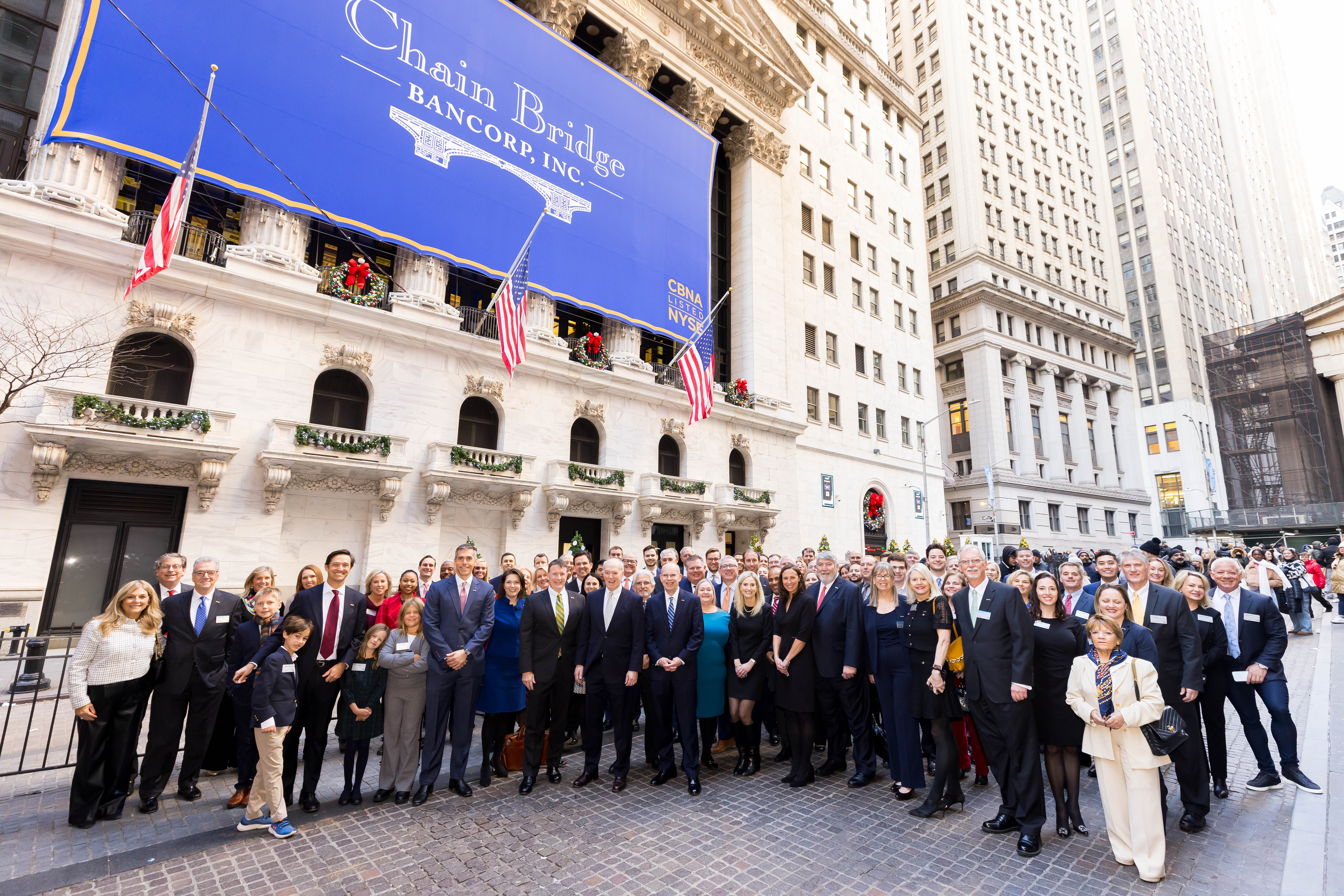 Chain Bridge directors, officers, employees, stockholders, and families gathered outside the New York Stock Exchange beneath a Chain Bridge Bancorp banner.